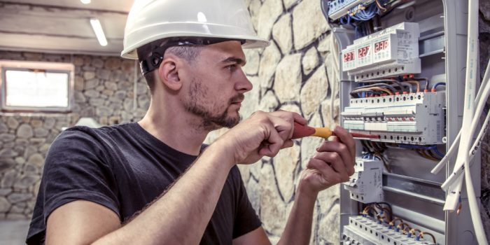 male-electrician-works-in-switchboard-with-an-electrical-connecting-cable male-electrician-works-in-switchboard-with-an-electrical-connecting-cable